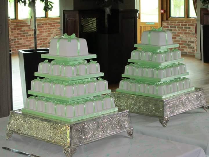 Two matching tiered displays of white and sage green mini wedding cakes on silver stands